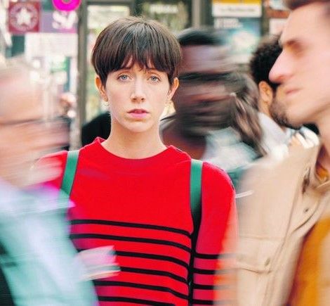 Una mujer mira de frente mientras otras personas borrosas pasan por su lado.