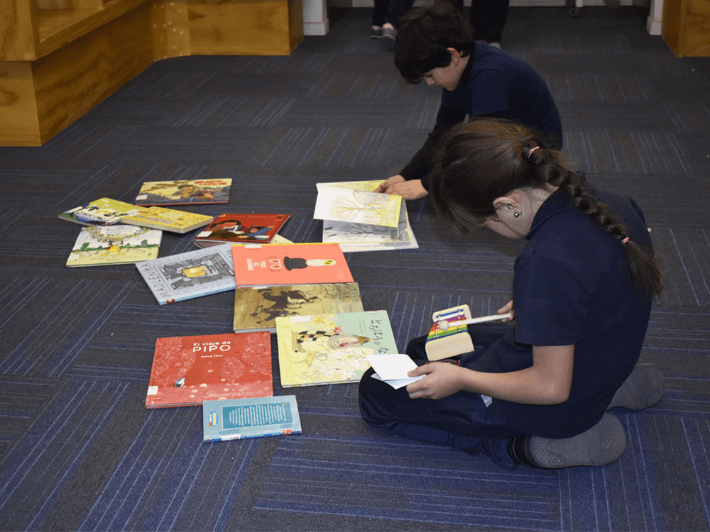 Fotografía con un niño y una niña revisando libros en el piso