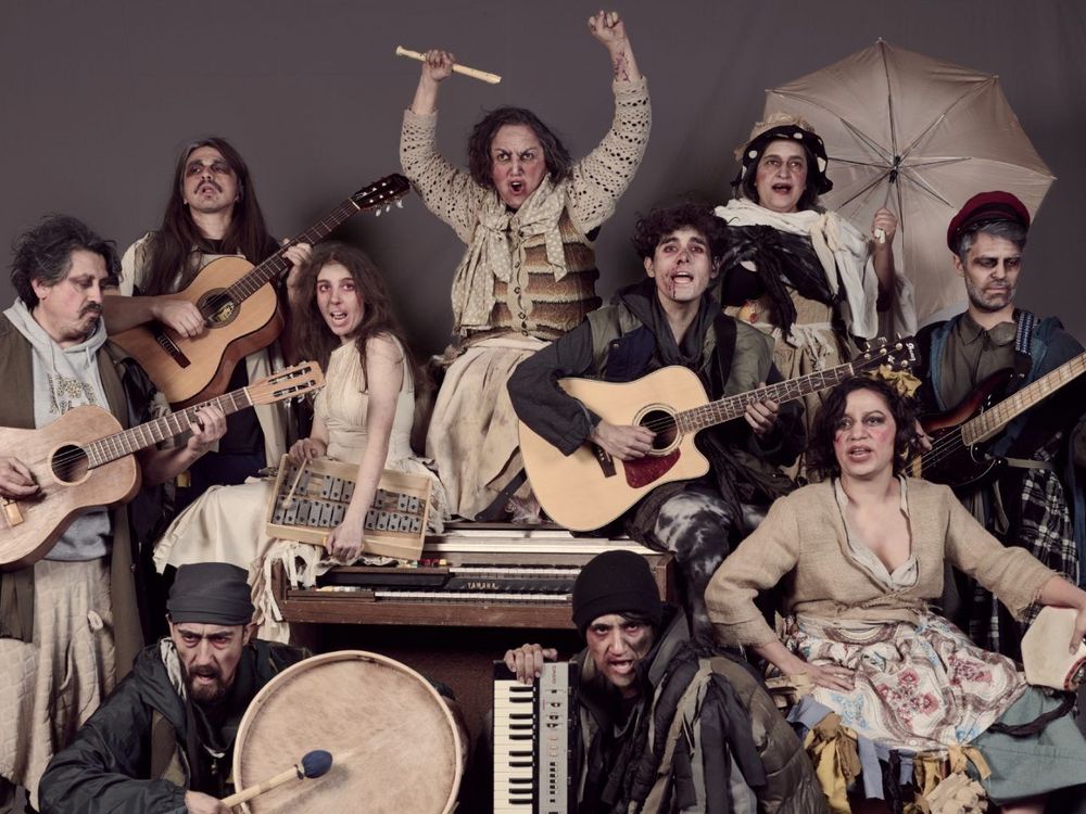 Plano general de muchos personajes posando para la foto. Estan vestidos con estropajos, desliñados y tienen multiples instrumentos musicales.