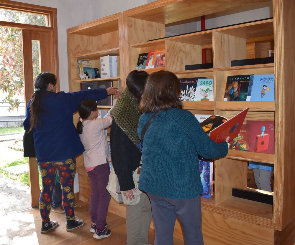 Imagen con personas mirando libros en un estante ubicado en una biblioteca