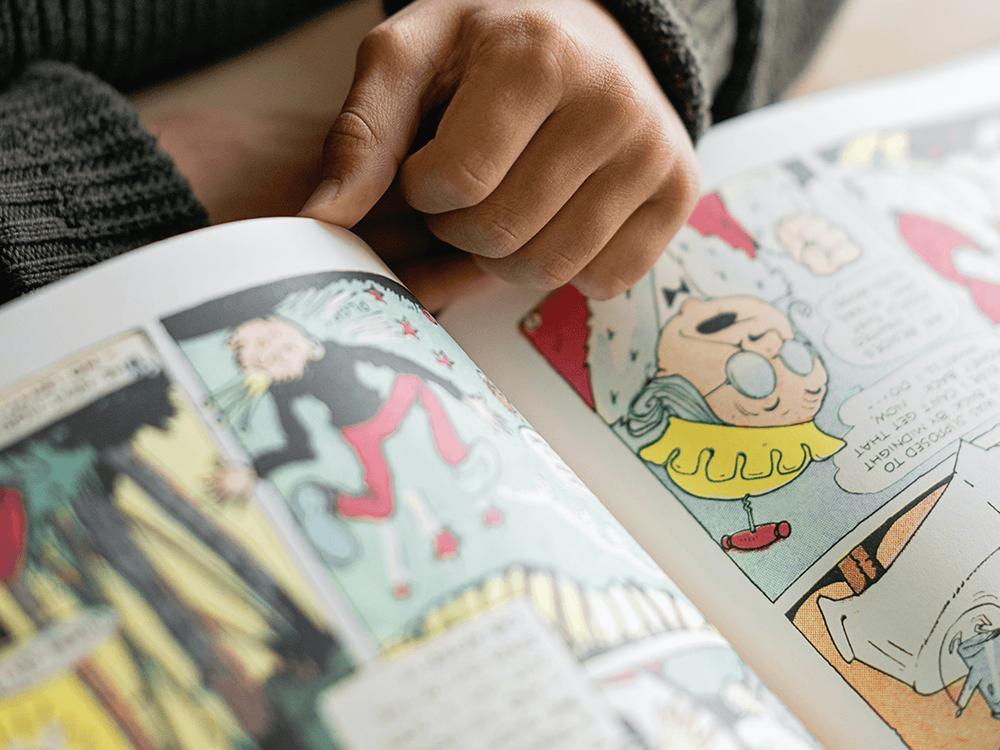 Fotografía de un libro grande de historietas siendo leído y tocado por una persona.