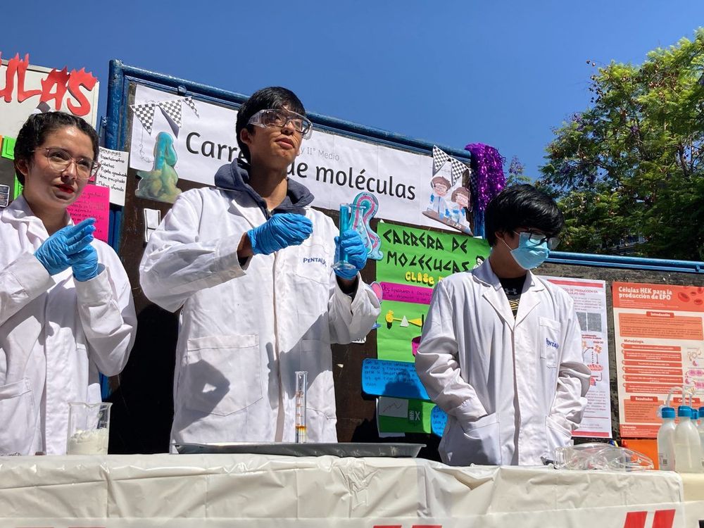 Plano general de estudiantes de quimica presentando un proyecto de ciancia. Están vestidos con batas y lentes protectivos.