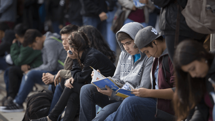 Jóvenes sentados en unos escalones. Dos de ellos miran un folleto de la UC