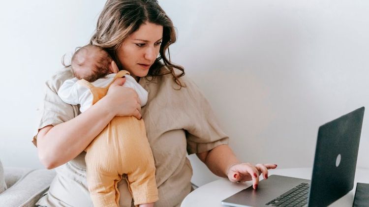 mamá cargando bebé y escribiendo en notebook