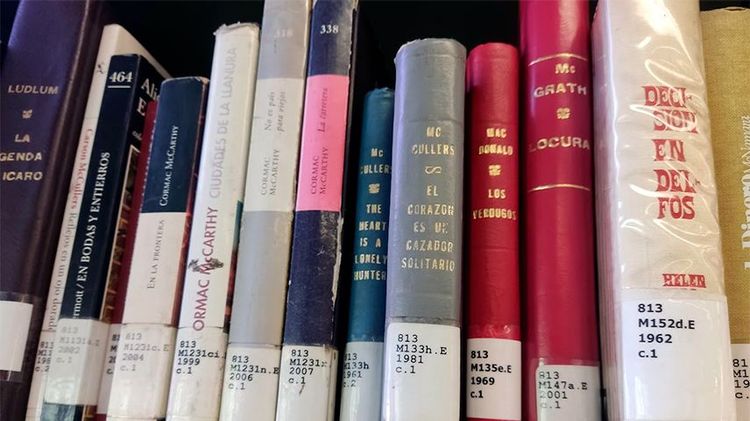 Fotografía de varios lomos de libros en una estantería de la biblioteca. Uno de ellos corresponde a "El corazón es un cazador solitario" de Carson McCullers